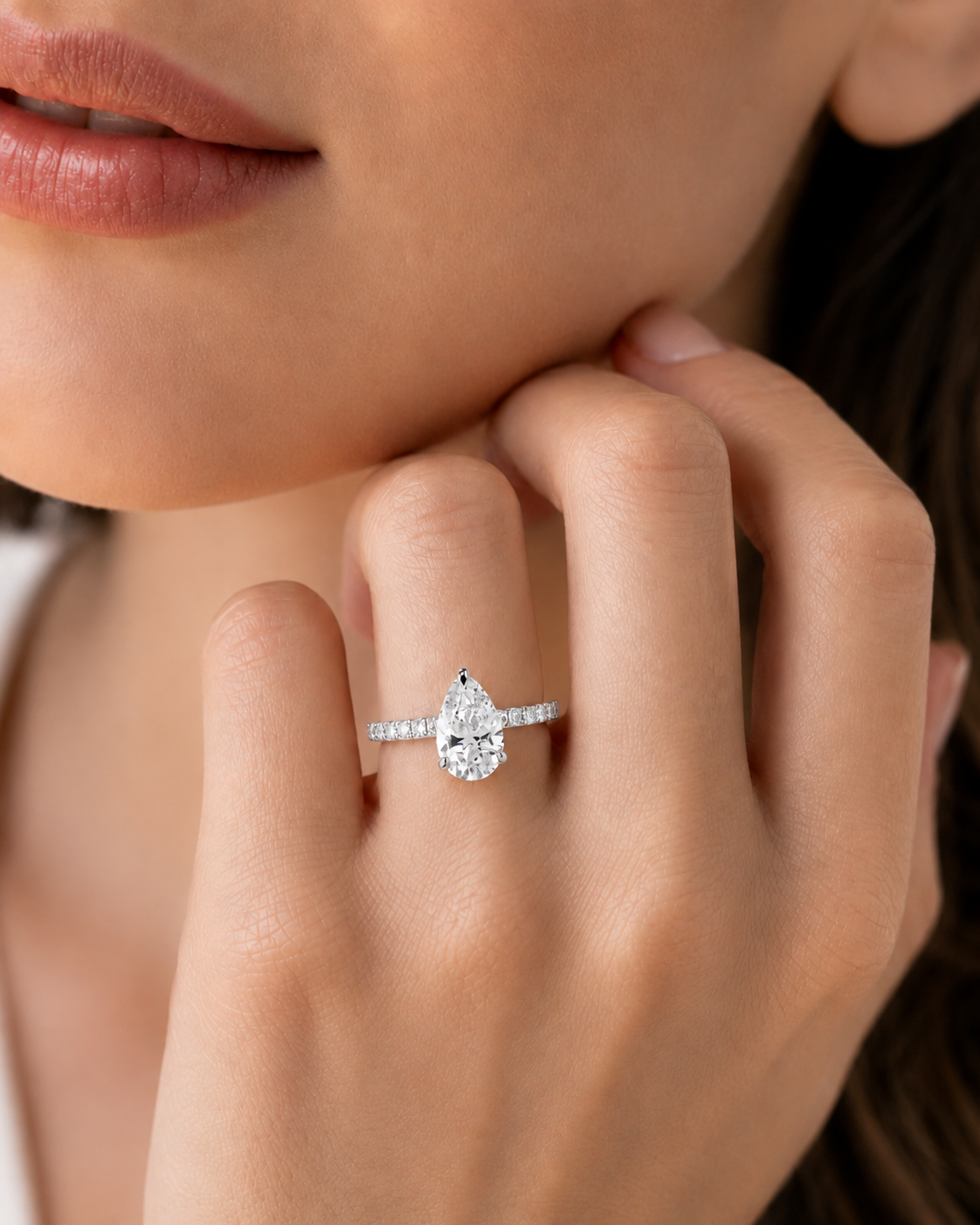 color_925_SIL,color_935_ARG,color_10K_WG, color_14K_WG &&A close-up lifestyle shot of a model wearing a silver ring with a pear-cut diamond and a row of smaller diamonds on the band.