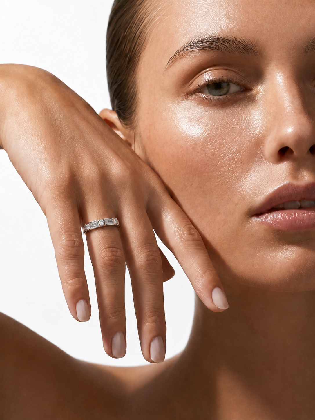 color_925_SIL,color_935_ARG,color_10K_WG, color_14K_WG &&A close-up lifestyle shot of a model wearing a delicate silver band ring with small clear stones on her ring finger, set against a clean white background.