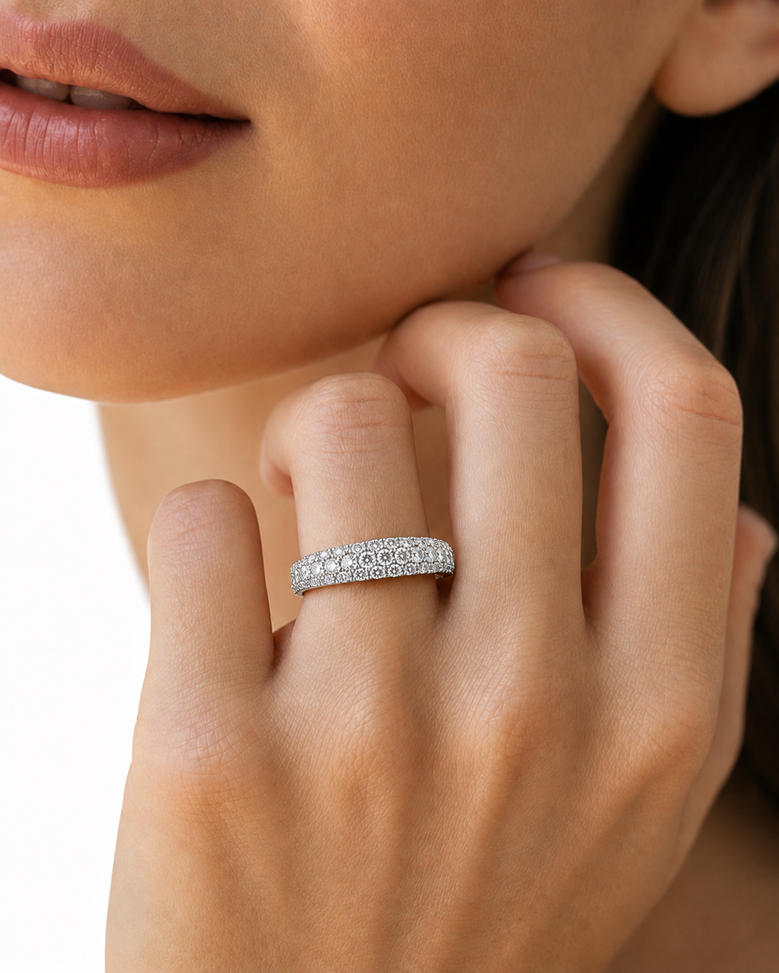 color_925_SIL,color_935_ARG,color_10K_WG, color_14K_WG &&A close-up lifestyle shot of a model wearing a diamond eternity band ring on her finger, with her hand resting near her chin against a clean white background.