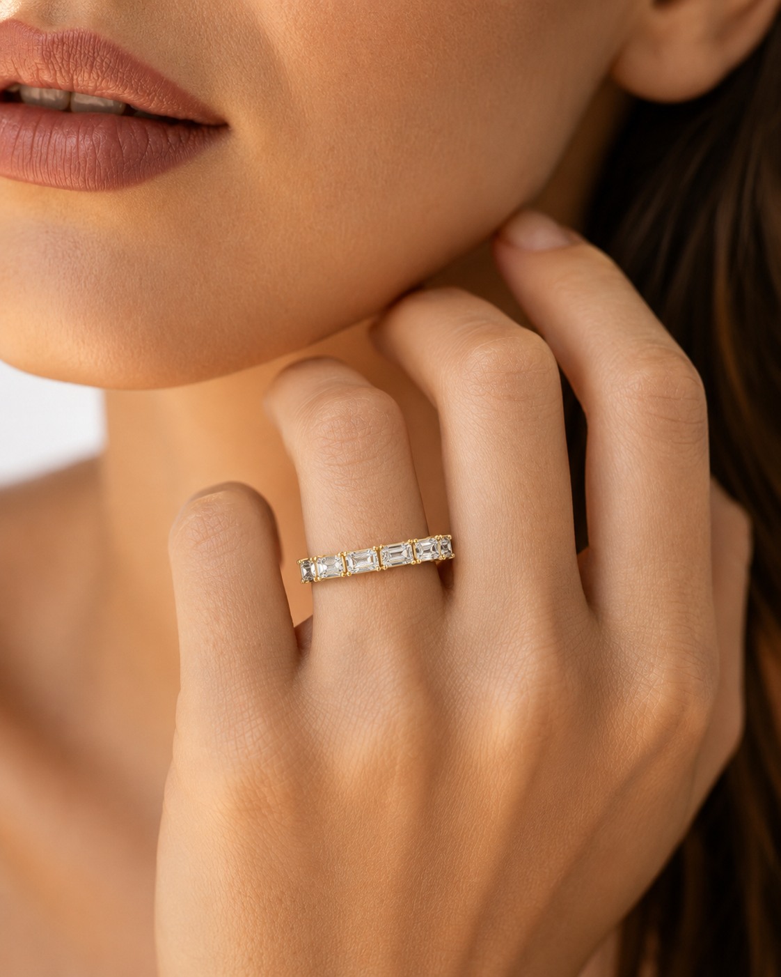 color_10K_YG, color_14K_YG &&A close-up lifestyle shot of a woman's hand wearing a delicate gold eternity ring set with small clear baguette-cut stones.