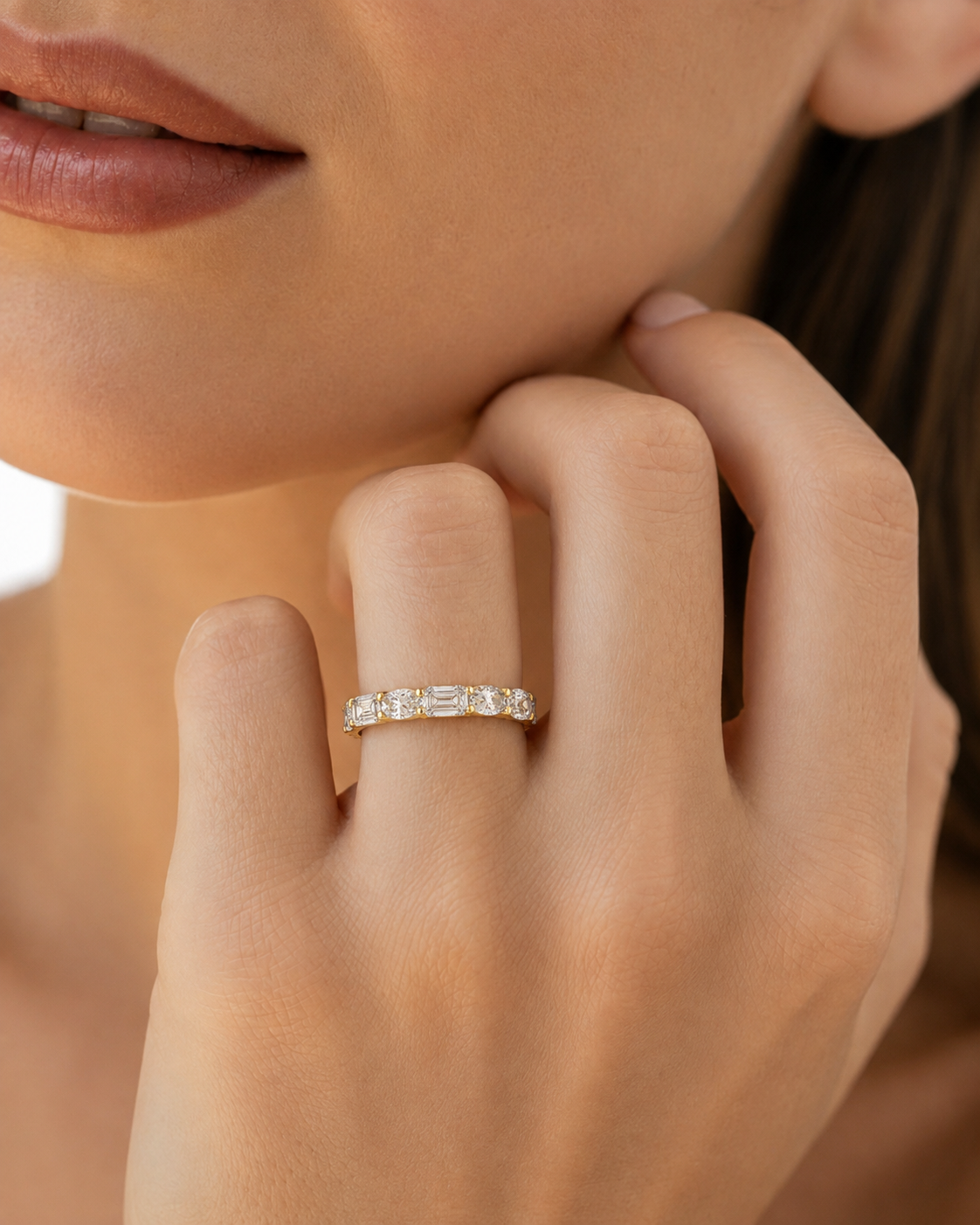 color_10K_YG, color_14K_YG &&A close-up of a model's hand wearing a delicate yellow gold eternity ring set with baguette-cut clear stones, set against a soft, warm neutral background.