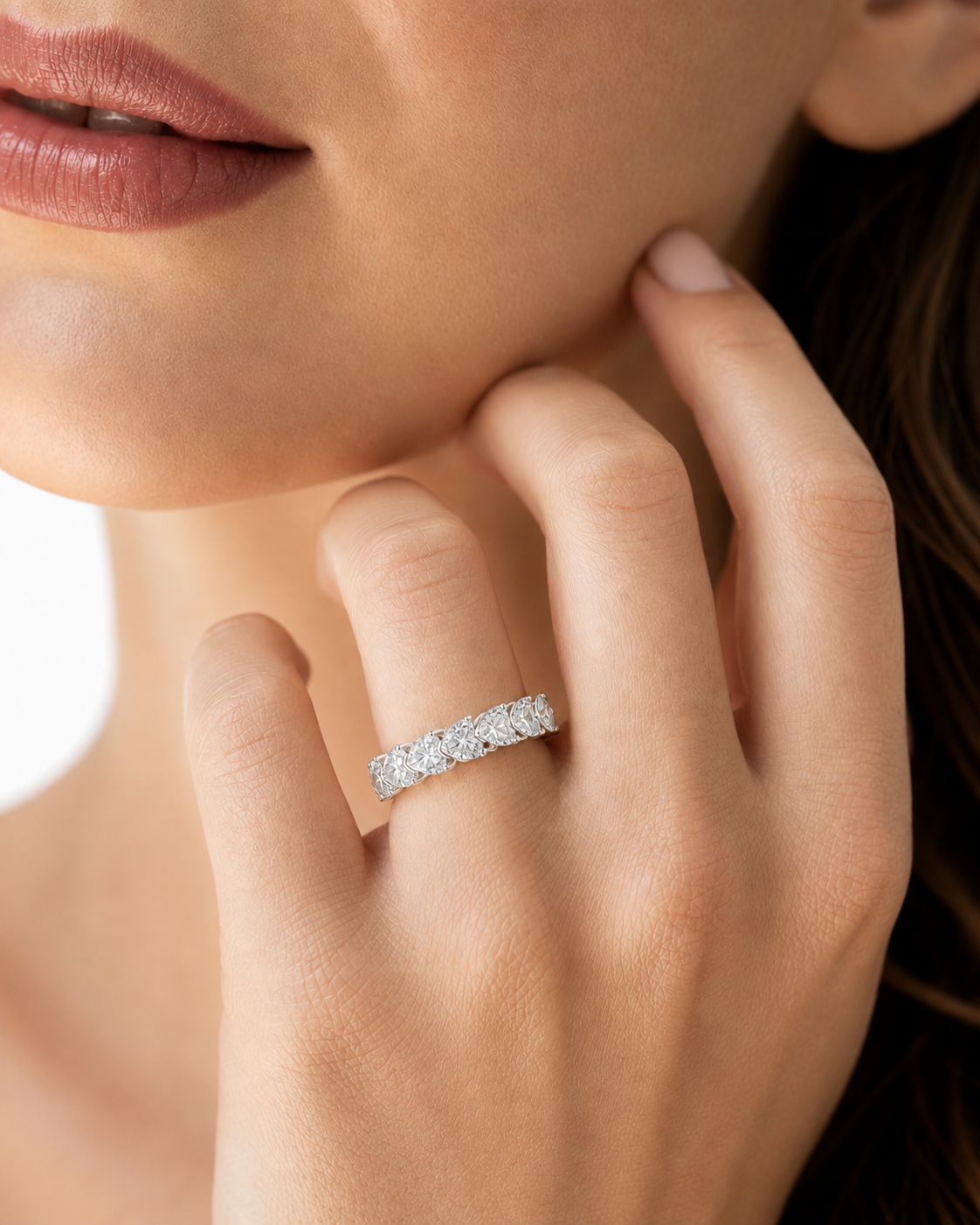color_925_SIL,color_935_ARG,color_10K_WG, color_14K_WG &&A close-up lifestyle shot of a model wearing a sparkling diamond eternity ring on her finger, with her hand resting near her chin.