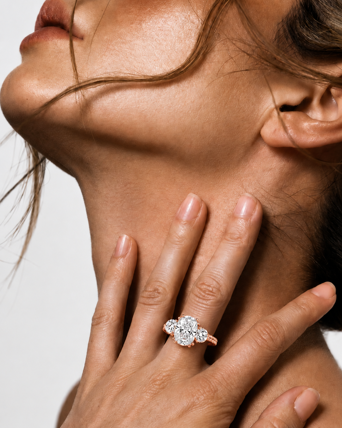 color_10K_RG, color_14K_RG &&A close-up lifestyle shot of a woman's neck and hand, wearing a rose gold ring with a clear diamond cluster setting on her ring finger.