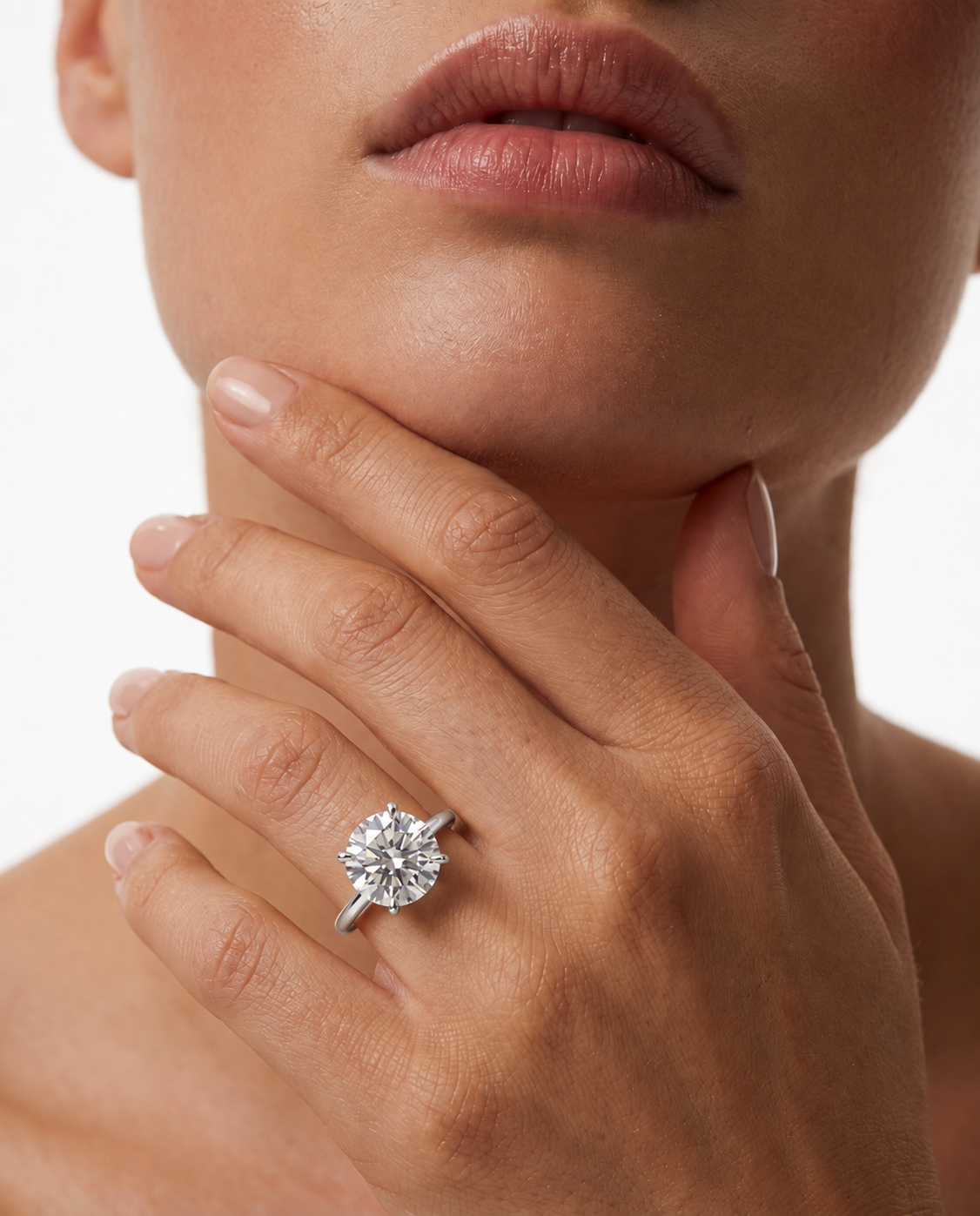 color_925_SIL,color_935_ARG,color_10K_WG, color_14K_WG &&A close-up of a model's hand and lower face wearing a silver-toned solitaire engagement ring with a round brilliant-cut diamond on a white background.