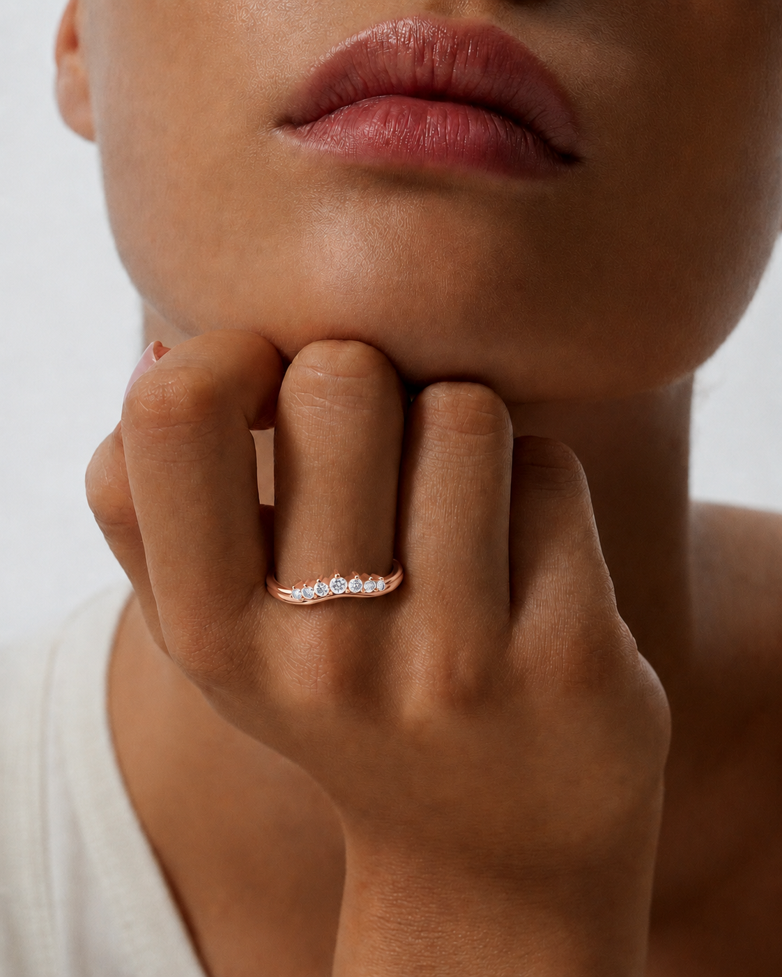 color_10K_RG, color_14K_RG &&A close-up of a model's hand resting on their chin, showcasing a delicate rose gold ring with a curved row of small clear gemstones.