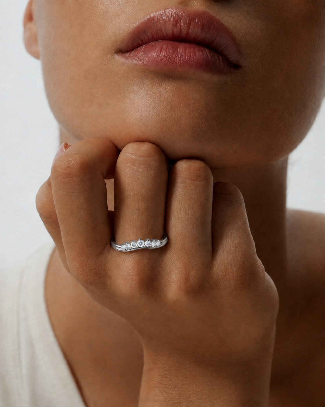 color_925_SIL,color_935_ARG,color_10K_WG, color_14K_WG &&A close-up lifestyle shot of a model wearing a delicate silver wave ring set with small clear stones on her finger.