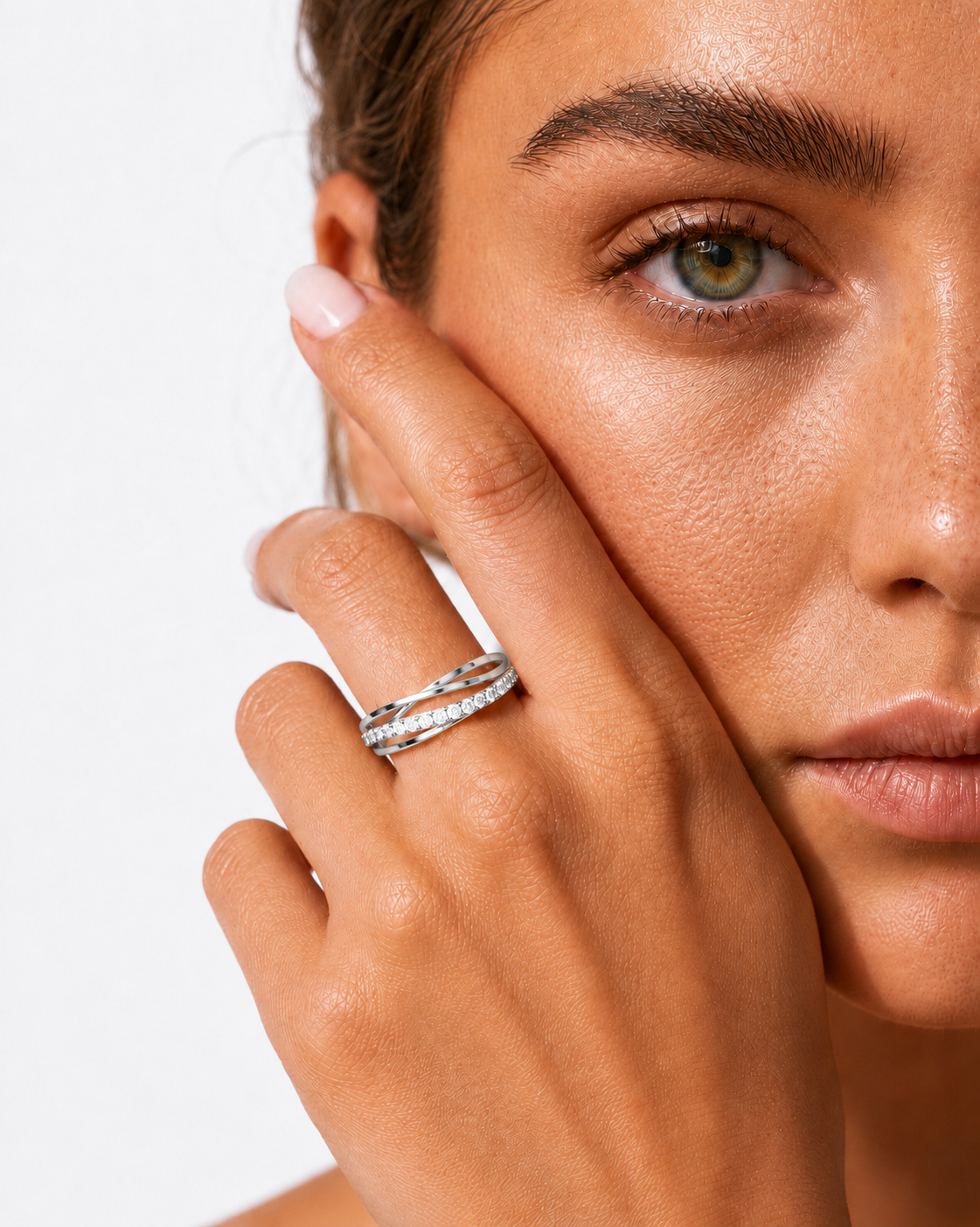 color_925_SIL,color_935_ARG,color_10K_WG, color_14K_WG &&A close-up of a model's hand and face wearing two stacked gold rings, one adorned with small clear stones, against a clean white background.