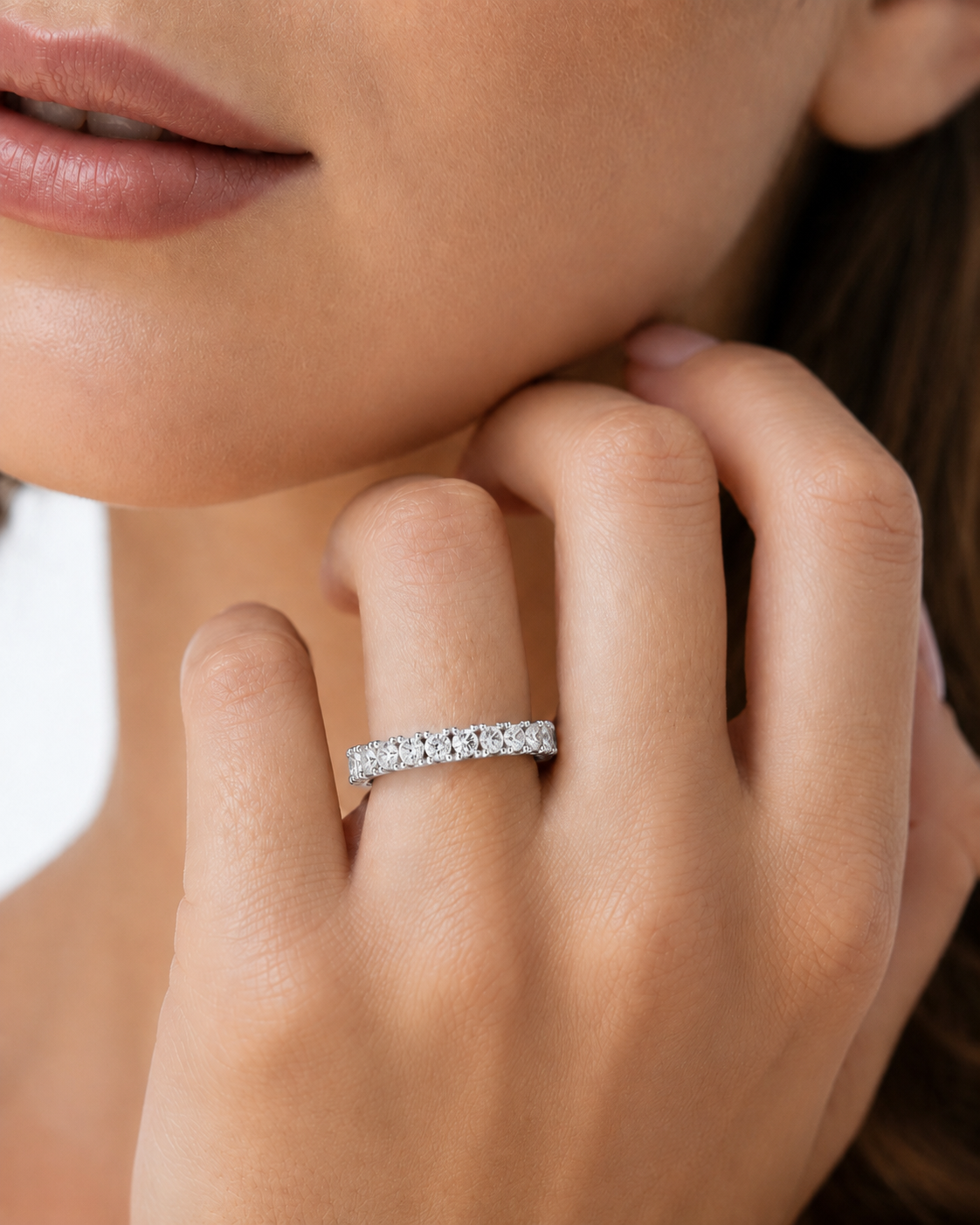 color_925_SIL,color_935_ARG,color_10K_WG, color_14K_WG &&A close-up of a woman's hand wearing a silver eternity ring set with small clear stones, with her lips and face partially visible in the frame.