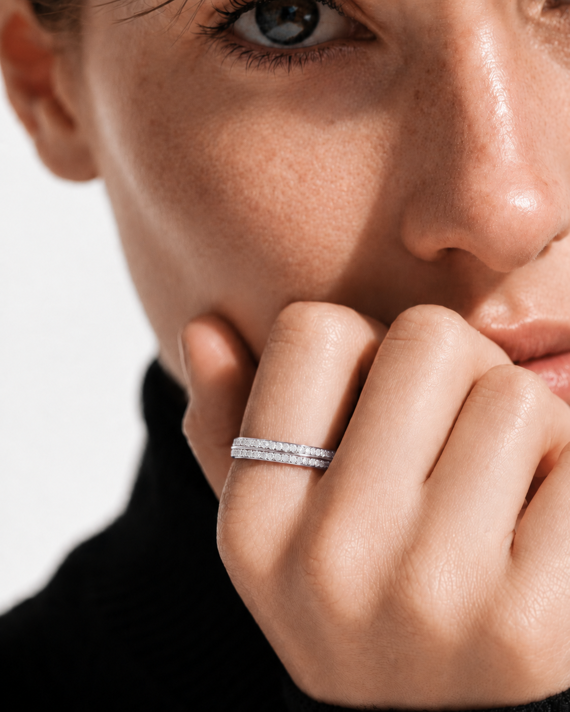 color_925_SIL,color_935_ARG,color_10K_WG, color_14K_WG &&A close-up lifestyle shot of a model wearing a delicate double-row diamond band ring on her finger, with her hand resting near her chin against a clean white background.