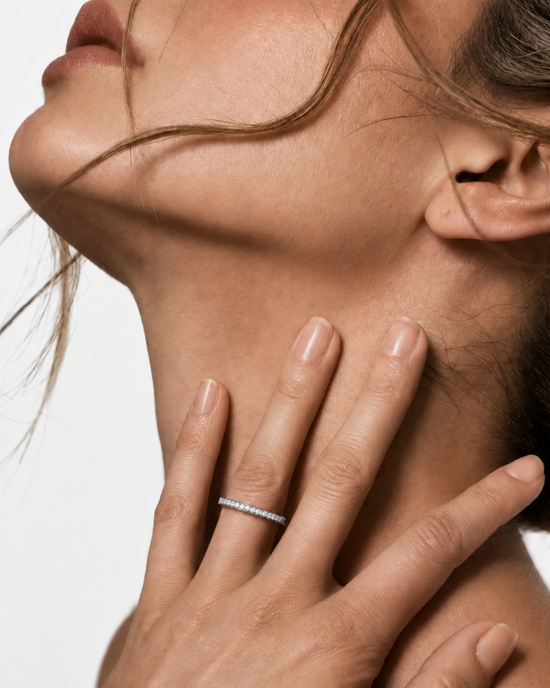 color_925_SIL,color_935_ARG,color_10K_WG, color_14K_WG &&A close-up lifestyle shot of a woman's neck and hand, wearing a thin silver band ring with a row of small clear gemstones on her ring finger, set against a clean white background.