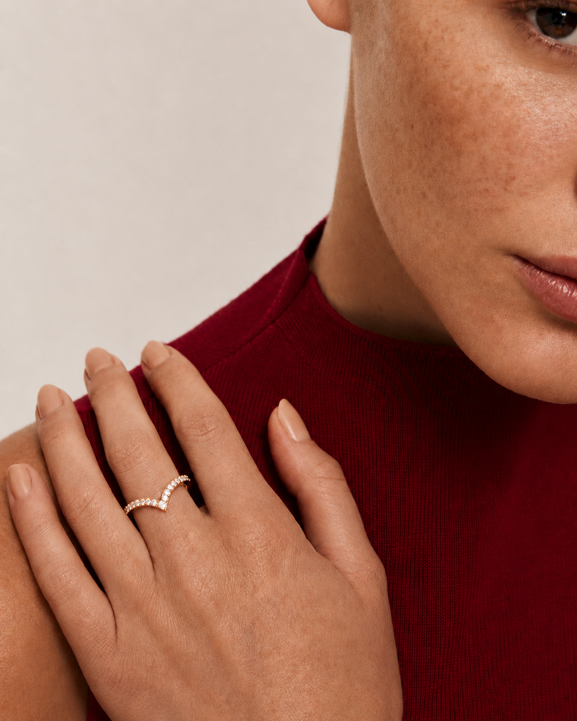 color_10K_RG, color_14K_RG &&A close-up lifestyle shot of a model wearing a delicate rose gold ring with a wavy, pavé-set diamond design on her finger. She is wearing a dark red ribbed knit top against a soft, light beige background.
