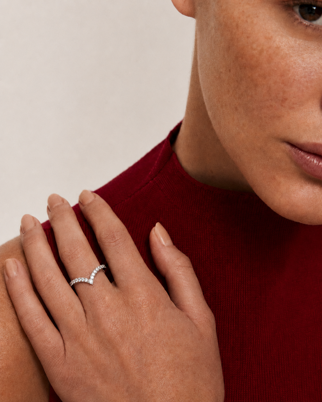 color_925_SIL,color_935_ARG,color_10K_WG, color_14K_WG &&A close-up lifestyle shot of a woman wearing a delicate silver ring with a wavy, pavé-set diamond design on her ring finger. She is wearing a dark red ribbed knit top against a neutral light beige background.