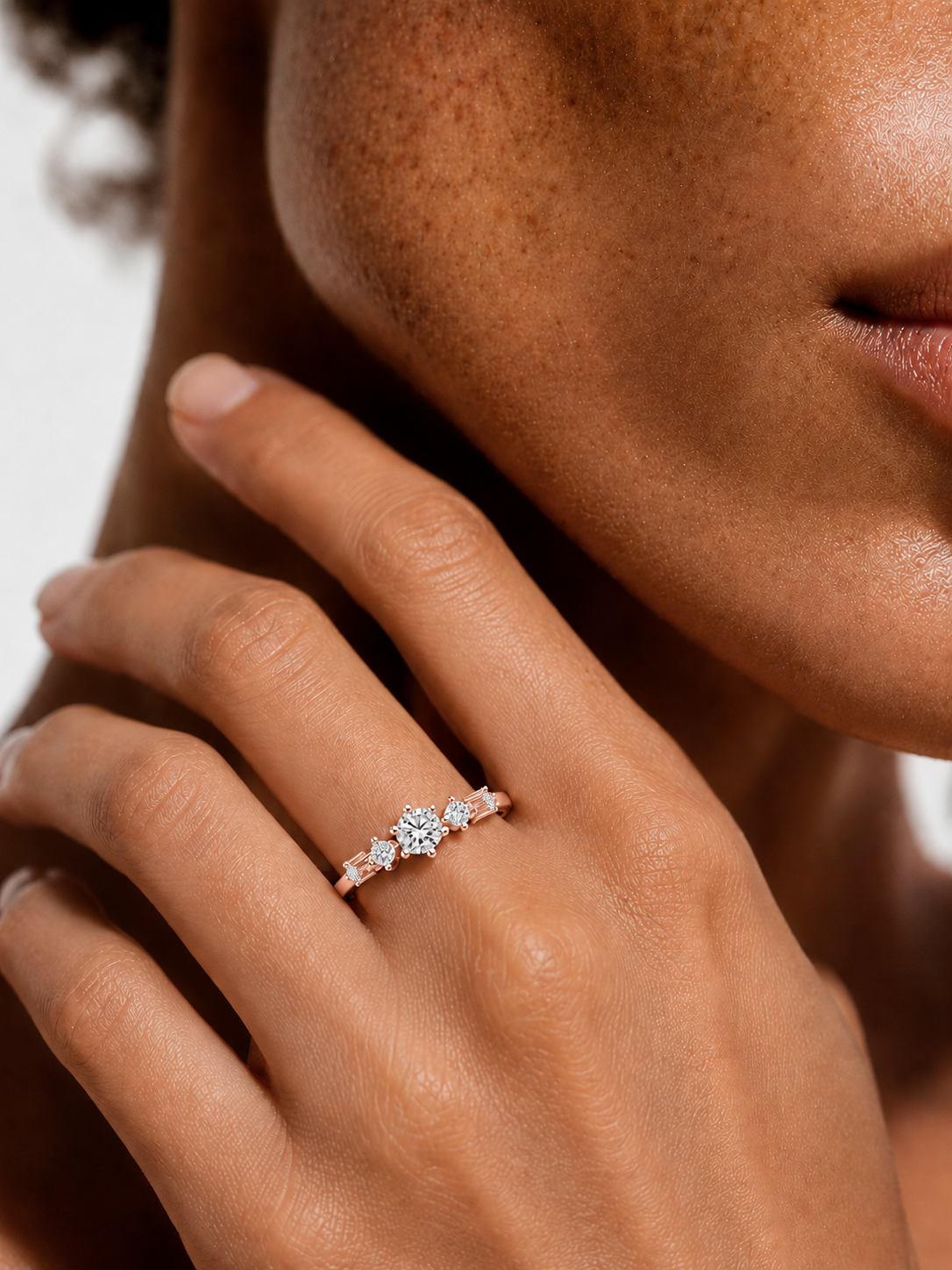 color_10K_RG, color_14K_RG &&A close-up lifestyle shot of a model's hand wearing a delicate rose gold ring with a central clear gemstone and small side stones.
