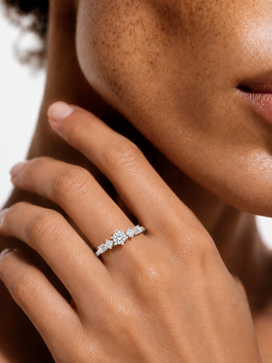 color_925_SIL,color_935_ARG,color_10K_WG, color_14K_WG &&A close-up lifestyle shot of a model's hand wearing a silver diamond ring with a marquise-cut center stone and smaller round diamonds on either side, set against a clean white background.