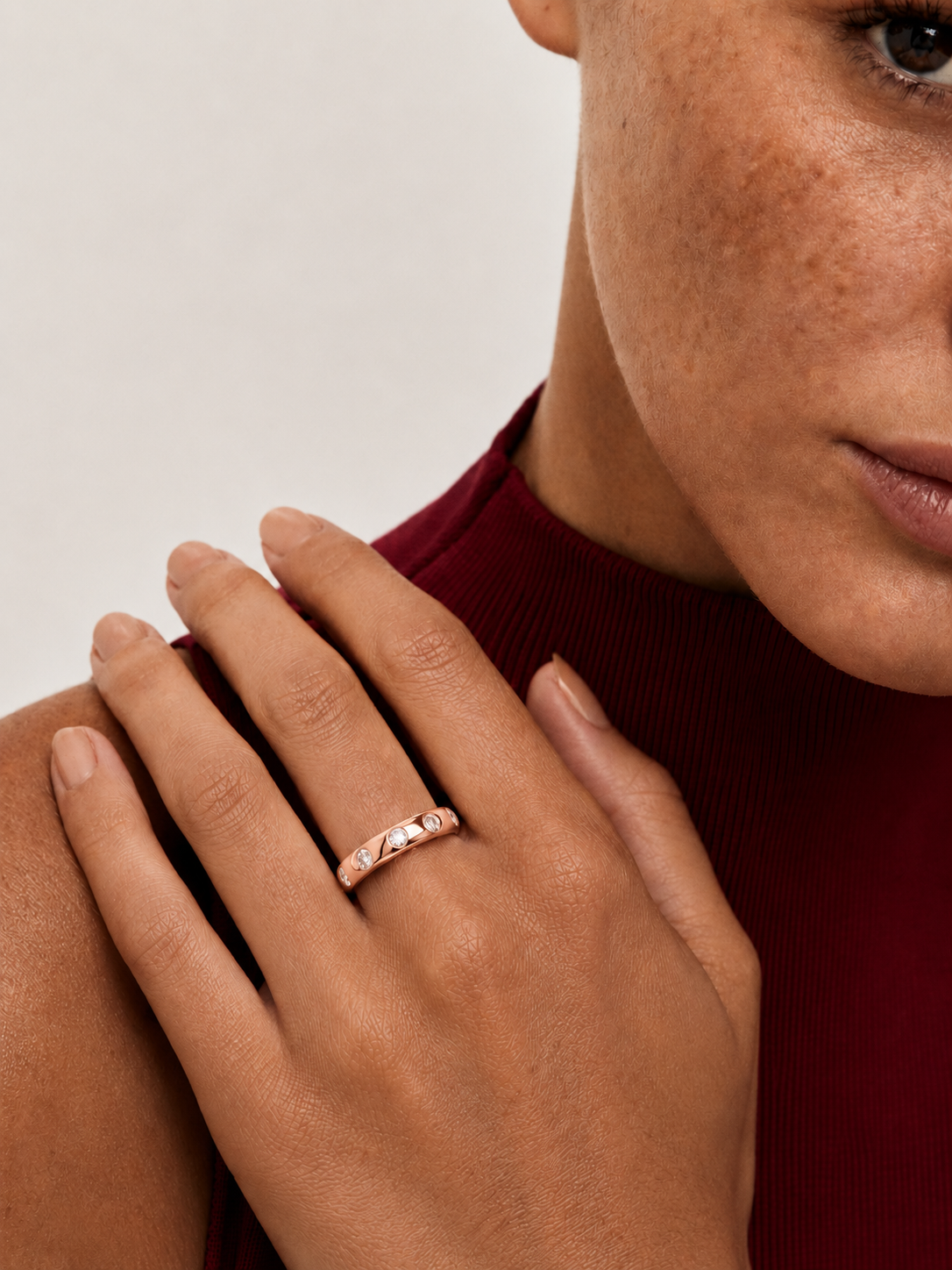 color_10K_RG, color_14K_RG &&A close-up lifestyle shot of a woman wearing a thin rose gold band ring with small clear stones, resting her hand on her shoulder.