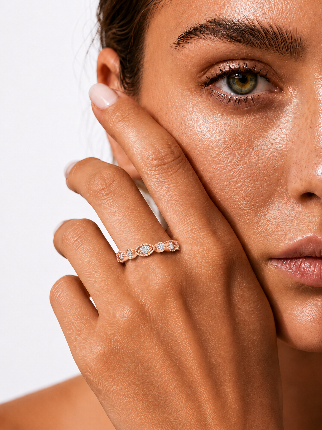 color_10K_RG, color_14K_RG &&A close-up lifestyle shot of a model wearing a delicate rose gold band ring with a row of small clear gemstones, with her hand resting against her cheek against a clean white background.