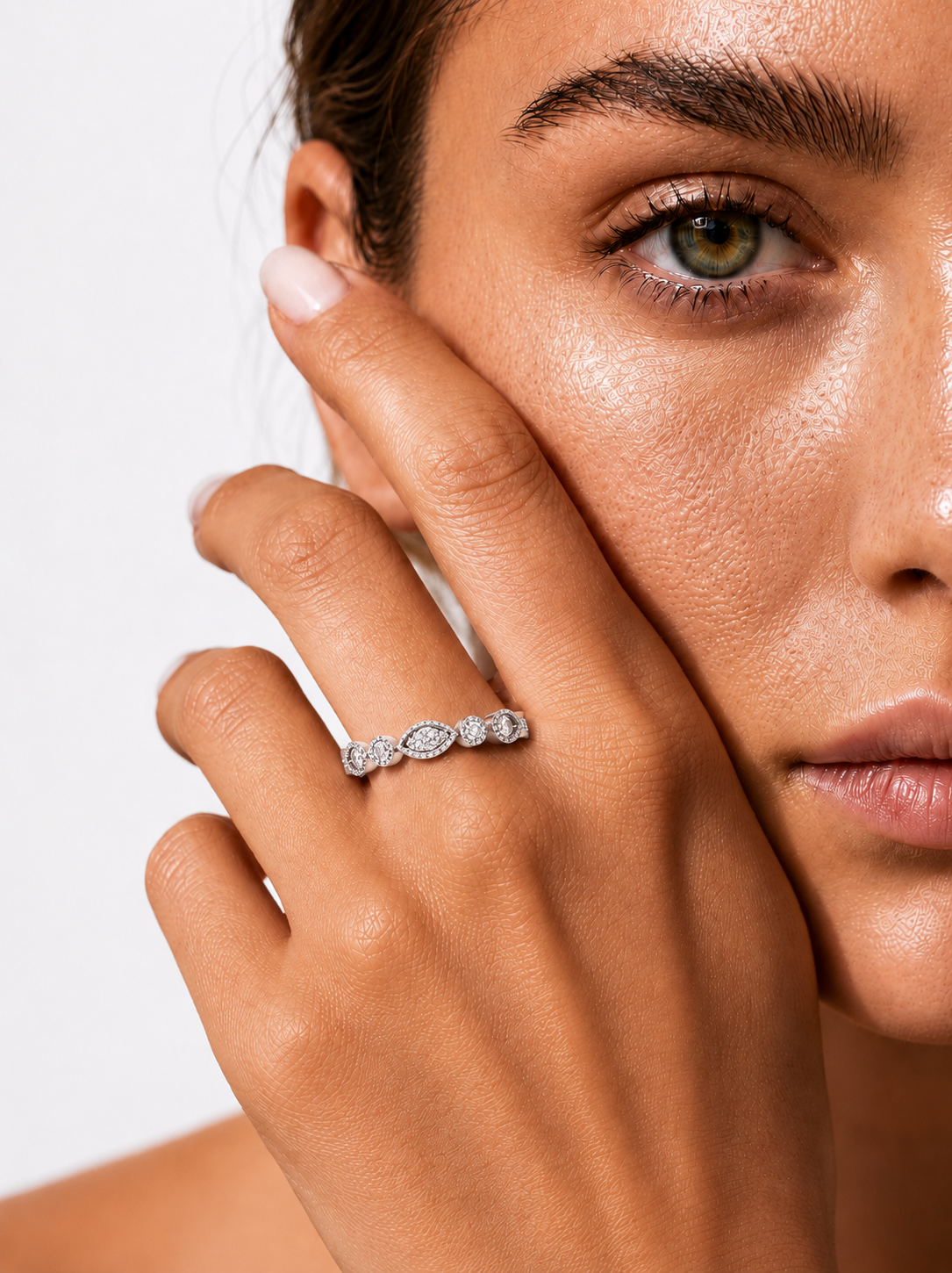 color_925_SIL,color_935_ARG,color_10K_WG, color_14K_WG &&A close-up lifestyle shot of a model wearing a delicate silver ring with a row of small clear marquise-cut gemstones. The model's face and hand are shown against a clean, light gray background.
