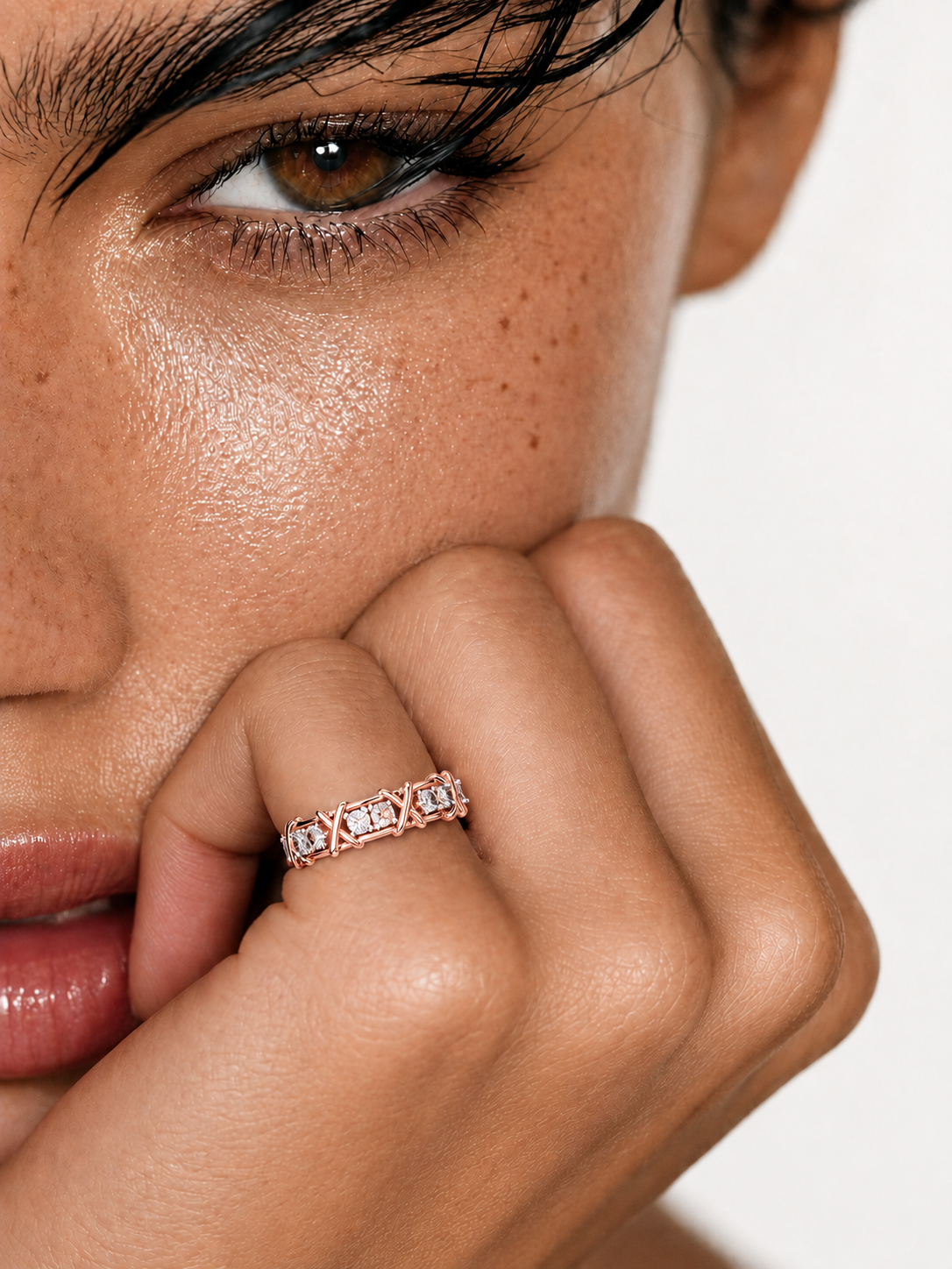 color_10K_RG, color_14K_RG &&A close-up lifestyle shot of a model wearing a delicate rose gold eternity ring with small clear stones on her finger, set against a clean white background.