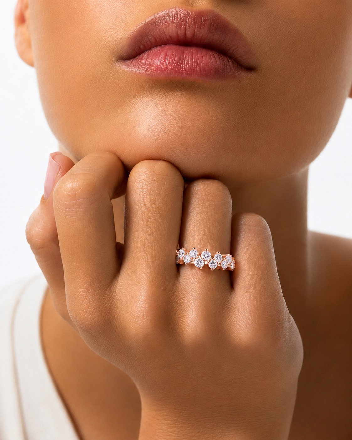 color_10K_RG, color_14K_RG &&A close-up lifestyle shot of a model's hand resting on their chin, wearing a delicate rose gold band ring adorned with small, sparkling clear gemstones.