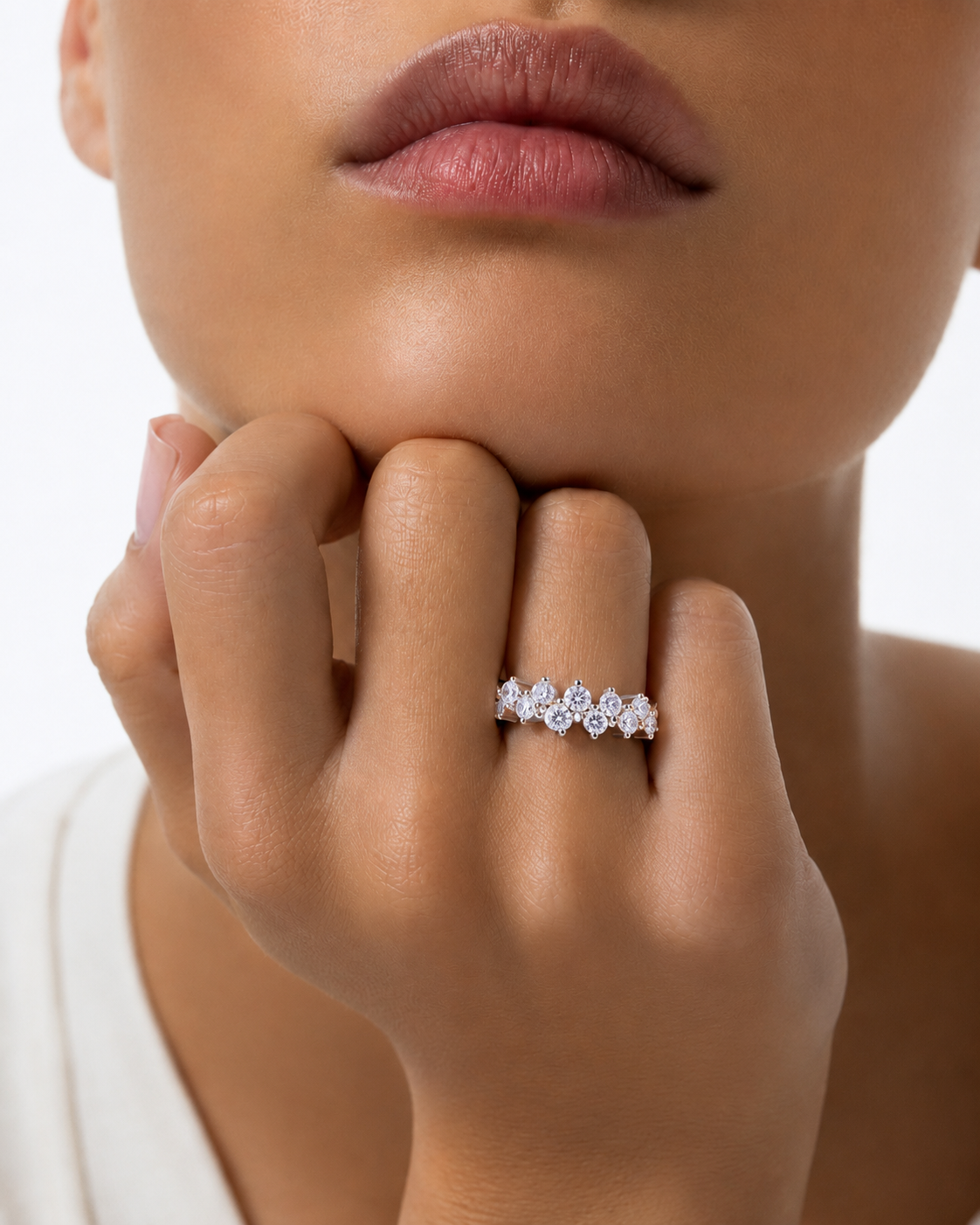 color_925_SIL,color_935_ARG,color_10K_WG, color_14K_WG &&A close-up lifestyle shot of a model wearing a delicate silver band ring adorned with small, clear floral-cut gemstones. The model's hand rests near her chin against a clean white background.