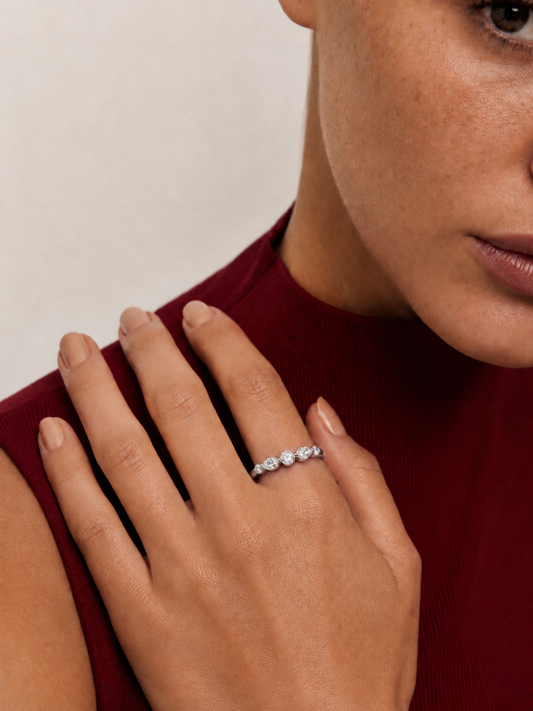 color_925_SIL,color_935_ARG,color_10K_WG, color_14K_WG &&A close-up lifestyle shot of a woman wearing a delicate silver ring with three small clear gemstones on her finger, set against a dark red ribbed top and a neutral light background.