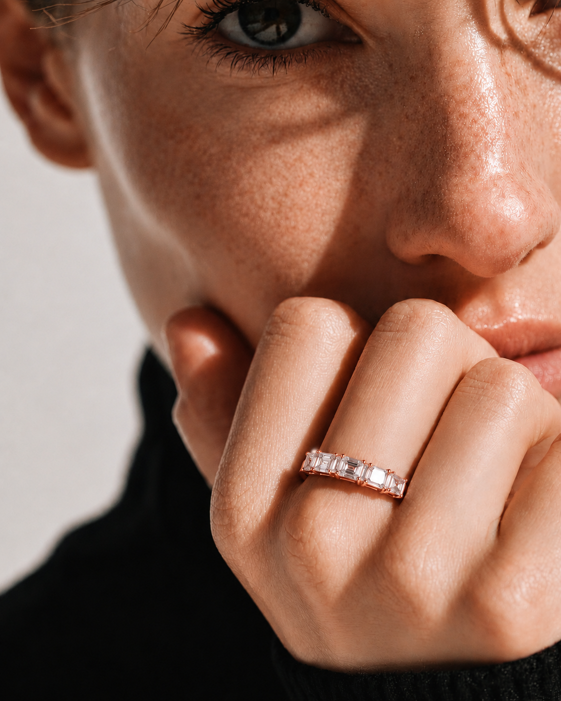color_10K_RG, color_14K_RG &&A close-up lifestyle shot of a model wearing a thin gold band ring set with small clear stones on her finger, with her hand resting near her chin against a neutral light background.