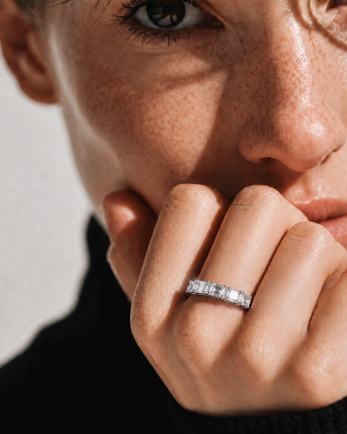 color_925_SIL,color_935_ARG,color_10K_WG, color_14K_WG &&A close-up lifestyle shot of a model wearing a silver band ring with rectangular clear stones on her finger. The image features dramatic, high-contrast natural lighting and a neutral light gray background.