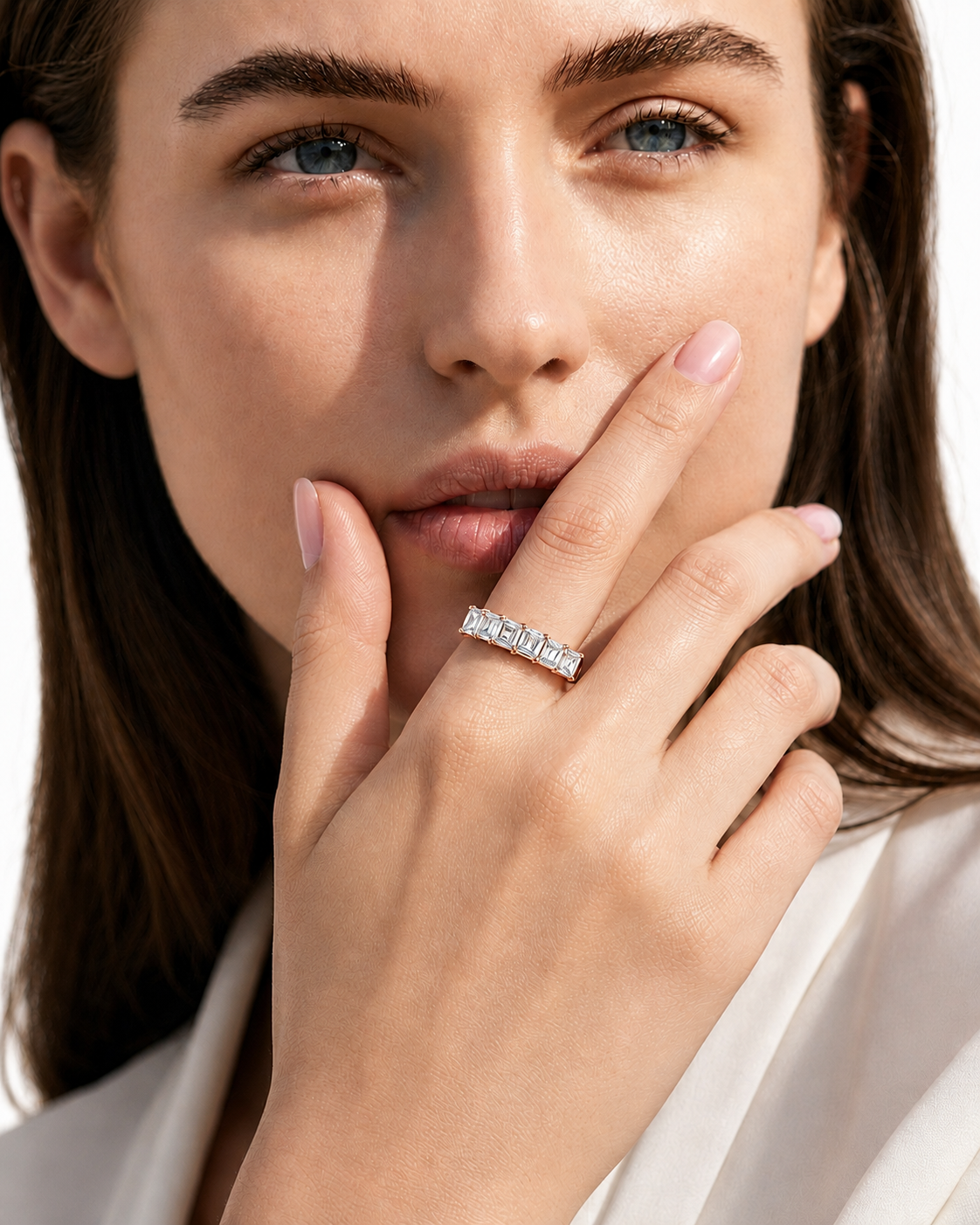 color_10K_RG, color_14K_RG &&A close-up lifestyle shot of a woman wearing a silver band ring with a row of clear baguette-cut gemstones. The ring is positioned on her ring finger, with her hand resting near her mouth.