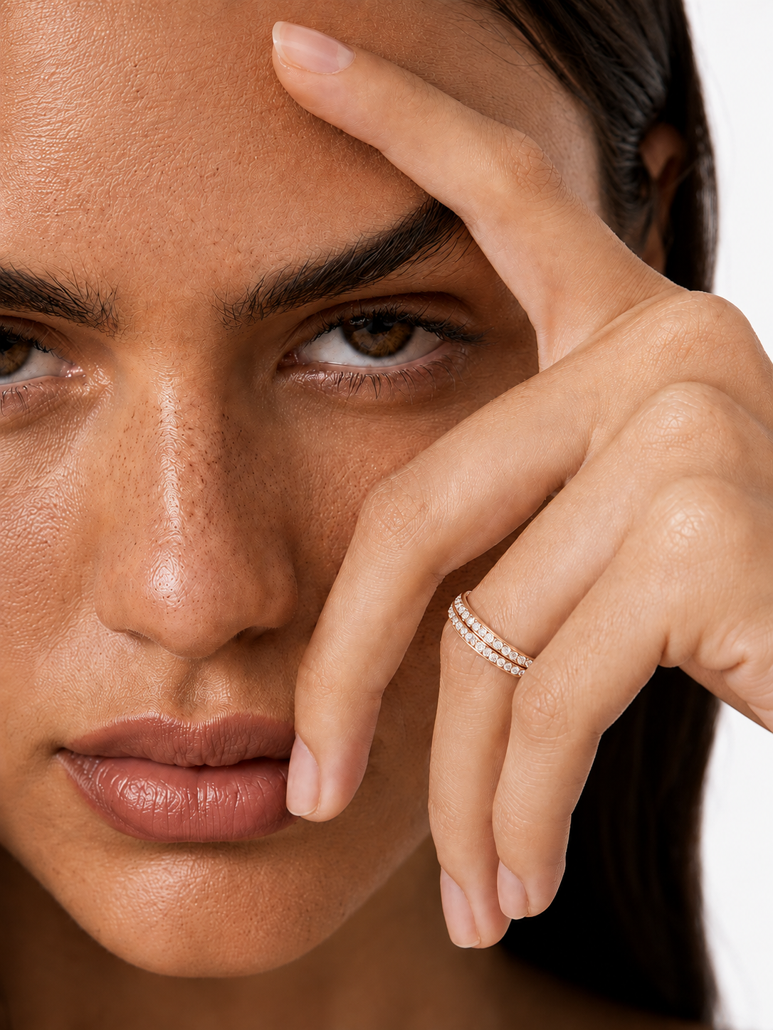 color_10K_RG, color_14K_RG &&A close-up lifestyle shot of a model wearing a delicate silver band ring with pavé-set clear stones on her ring finger, with her hand resting near her face against a clean white background.
