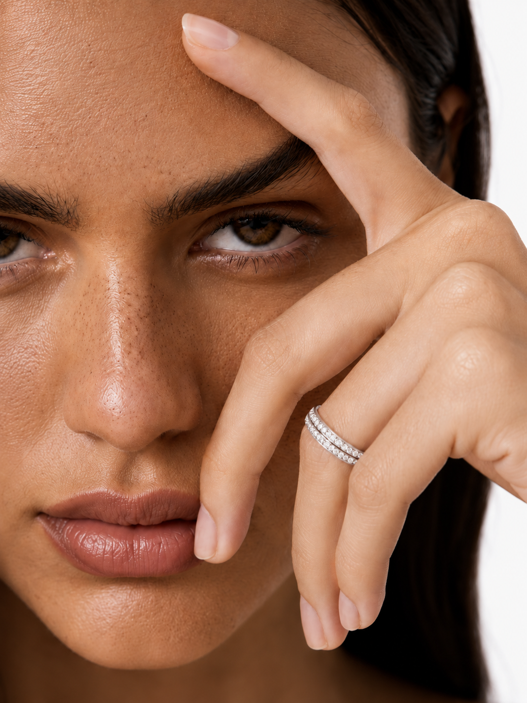 color_925_SIL,color_935_ARG,color_10K_WG, color_14K_WG &&A close-up lifestyle shot of a model wearing a delicate silver band ring with pavé-set clear stones on her ring finger, with her hand resting near her face against a clean white background.