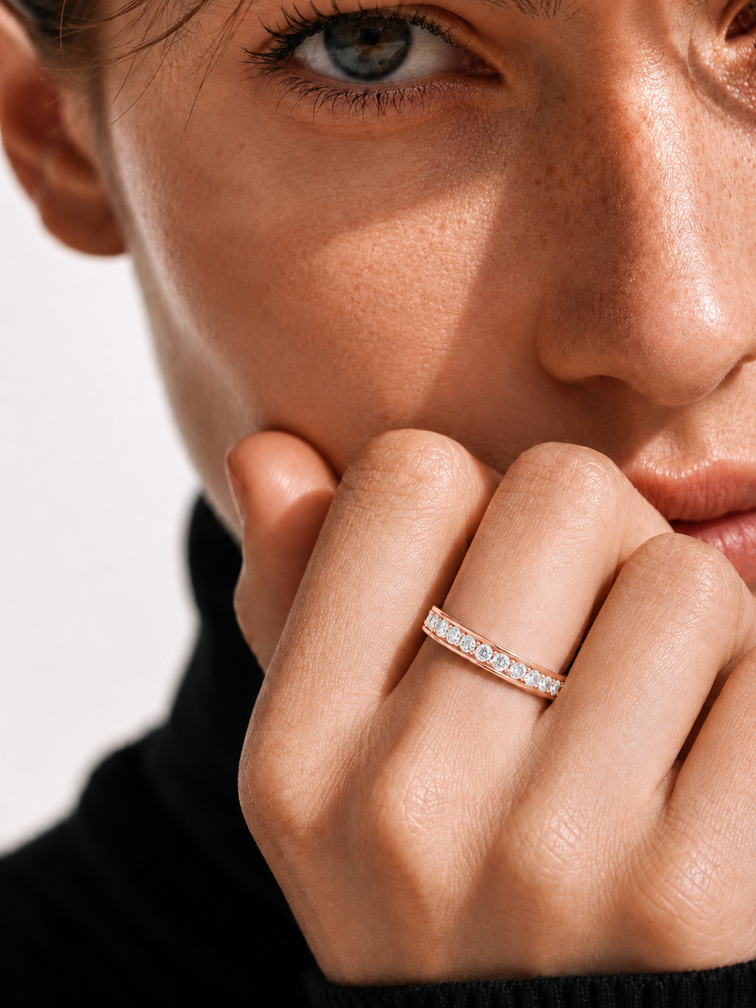 color_10K_RG, color_14K_RG &&A close-up lifestyle shot of a model wearing a delicate rose gold eternity ring set with small clear stones on her finger.