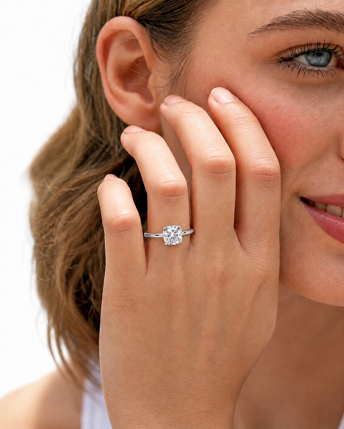 color_925_SIL,color_935_ARG,color_10K_WG, color_14K_WG &&A close-up lifestyle shot of a woman wearing a rose gold engagement ring with a round-cut clear gemstone on her finger, with her hand resting against her cheek against a white background.