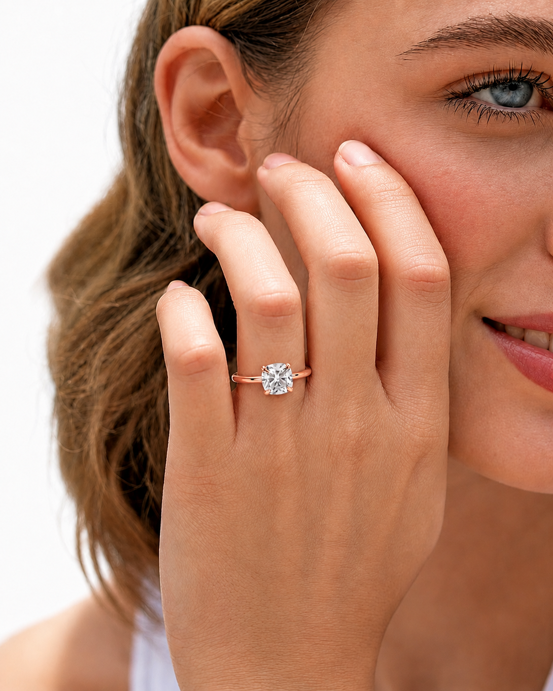 color_10K_RG, color_14K_RG &&A close-up lifestyle shot of a woman wearing a rose gold engagement ring with a round brilliant-cut diamond. The ring is shown on her finger, with her hand resting against her cheek, set against a clean white background.
