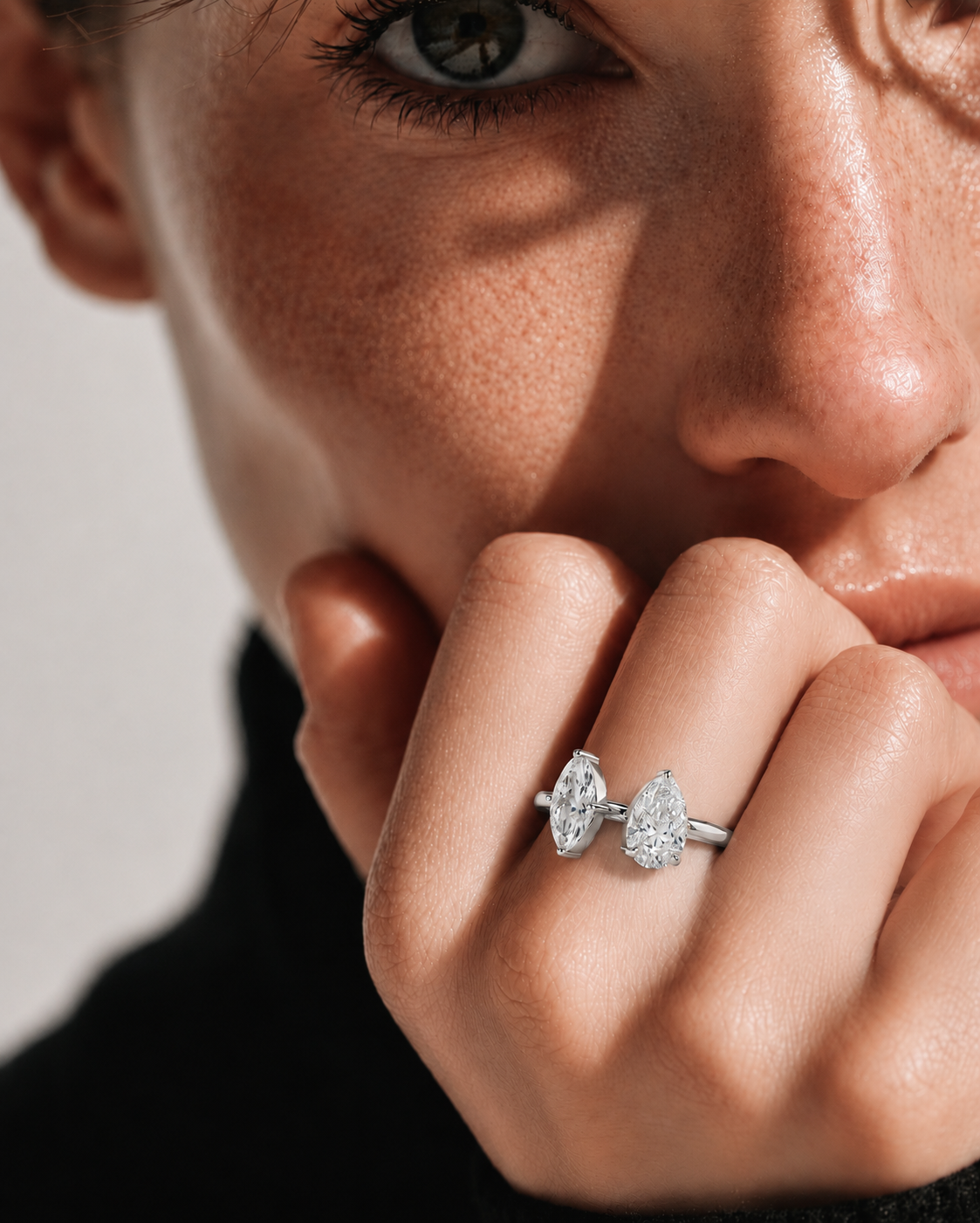 color_925_SIL,color_935_ARG,color_10K_WG, color_14K_WG &&A close-up lifestyle shot of a model wearing a silver ring with two marquise-cut clear gemstones, resting on her finger near her chin.
