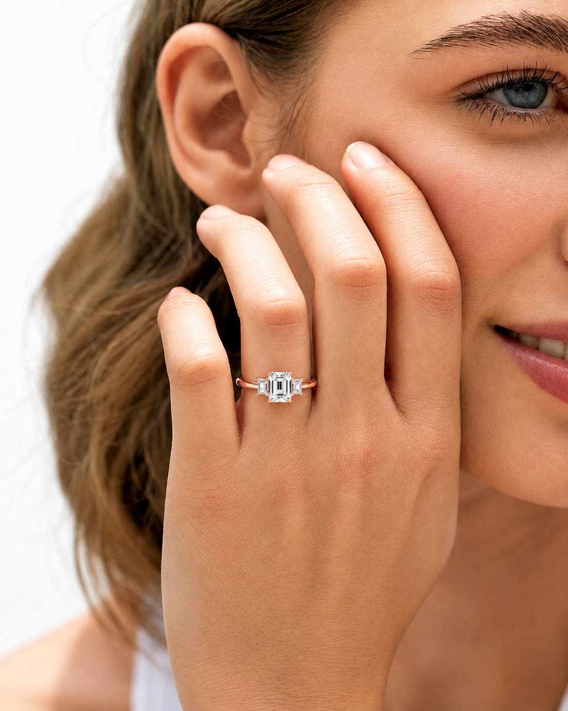 color_10K_RG, color_14K_RG &&A close-up lifestyle shot of a woman wearing a rose gold ring with a square-cut clear gemstone on her finger, with her hand resting against her cheek.