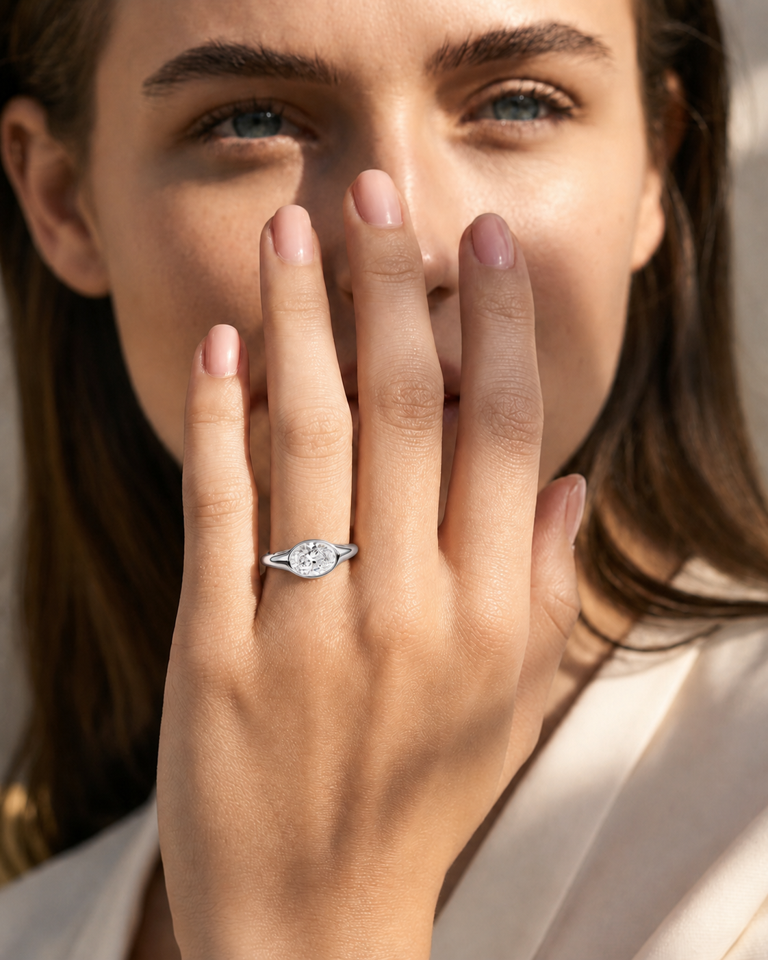 color_925_SIL,color_935_ARG,color_10K_WG, color_14K_WG &&A close-up lifestyle shot of a woman wearing a silver-toned ring with a marquise-cut clear gemstone on her finger, with her hand covering part of her face.