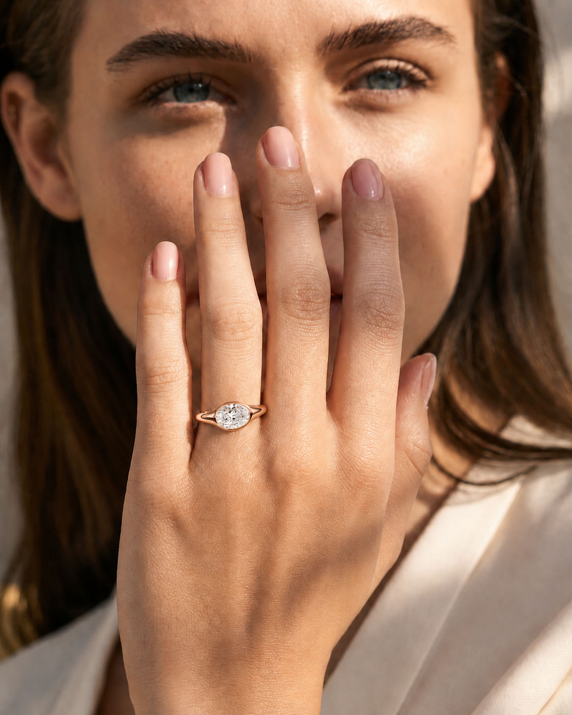 color_10K_RG, color_14K_RG &&A close-up lifestyle shot of a woman wearing a silver-toned ring with a marquise-cut clear gemstone on her finger, with her hand covering part of her face.