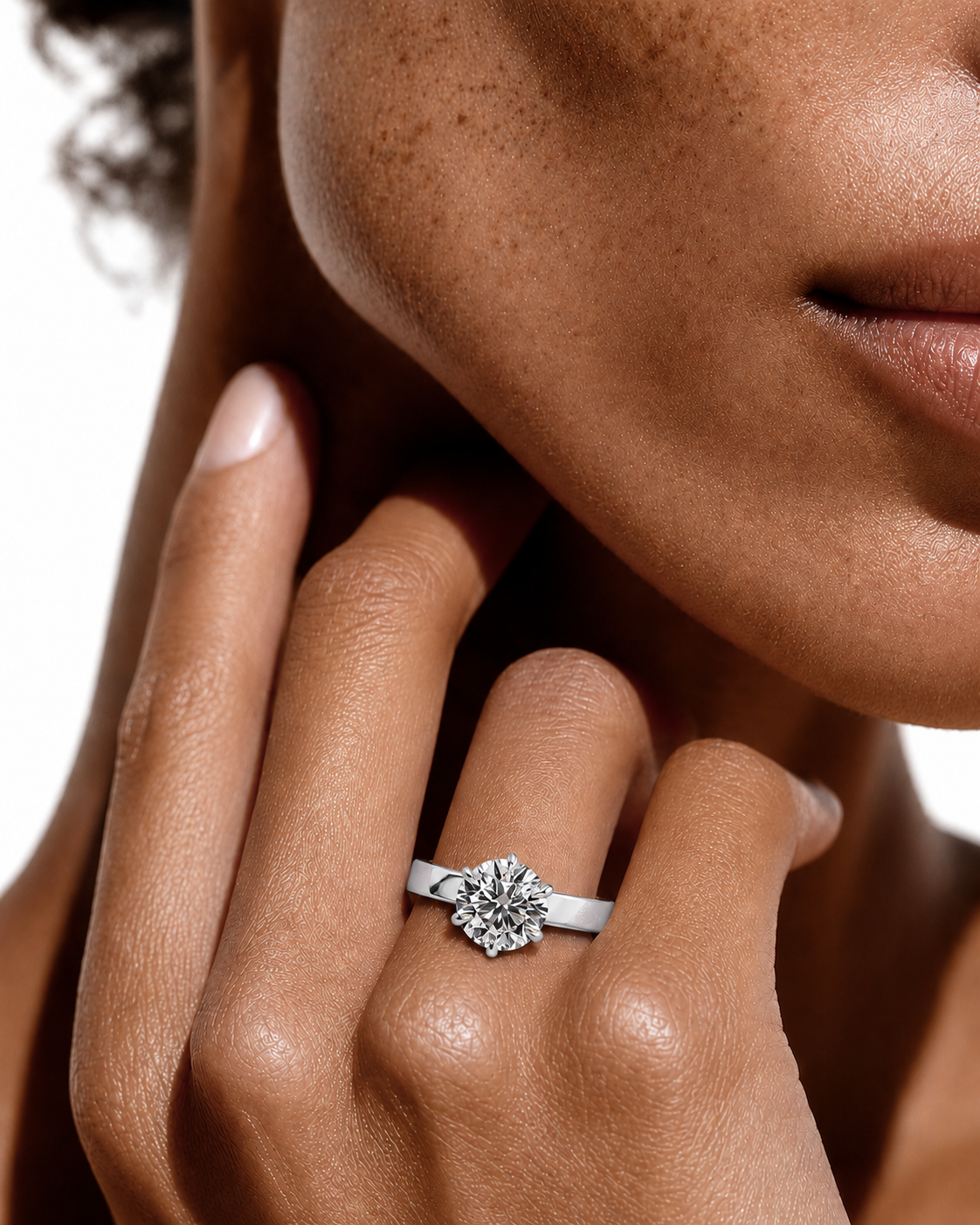 color_925_SIL,color_935_ARG,color_10K_WG, color_14K_WG &&A close-up lifestyle shot of a model's hand and lower face, showcasing a silver-toned diamond ring with a round cluster centerstone on the ring finger.