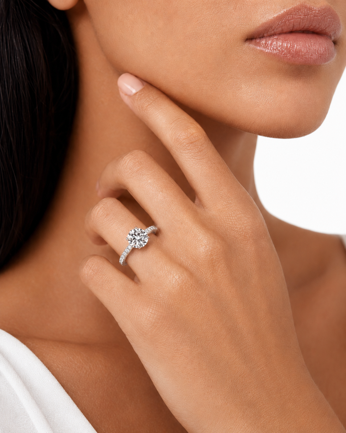 color_925_SIL,color_935_ARG,color_10K_WG, color_14K_WG &&A close-up lifestyle shot of a model wearing a silver-toned diamond engagement ring on her finger, with her hand resting near her chin against a clean white background.