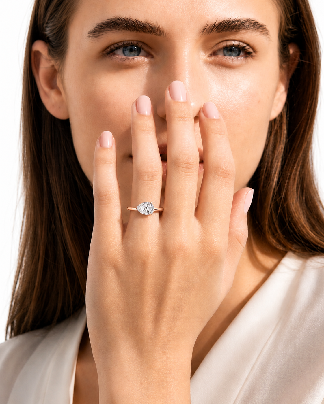 color_10K_RG, color_14K_RG &&A close-up lifestyle shot of a woman wearing a delicate gold ring with a small clear gemstone on her finger, holding her hand near her face against a clean white background.