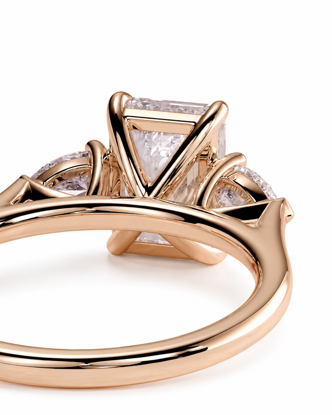 color_10K_RG, color_14K_RG &&A close-up of a rose gold ring featuring a large rectangular clear gemstone in a geometric setting, with smaller round clear gemstones on either side, shown on a white background.