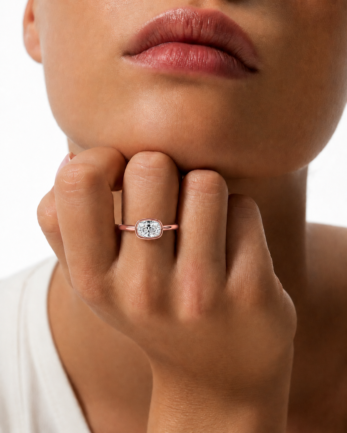 color_10K_RG, color_14K_RG &&A close-up lifestyle shot of a model wearing a rose gold ring with a bezel-set round clear gemstone on her finger.