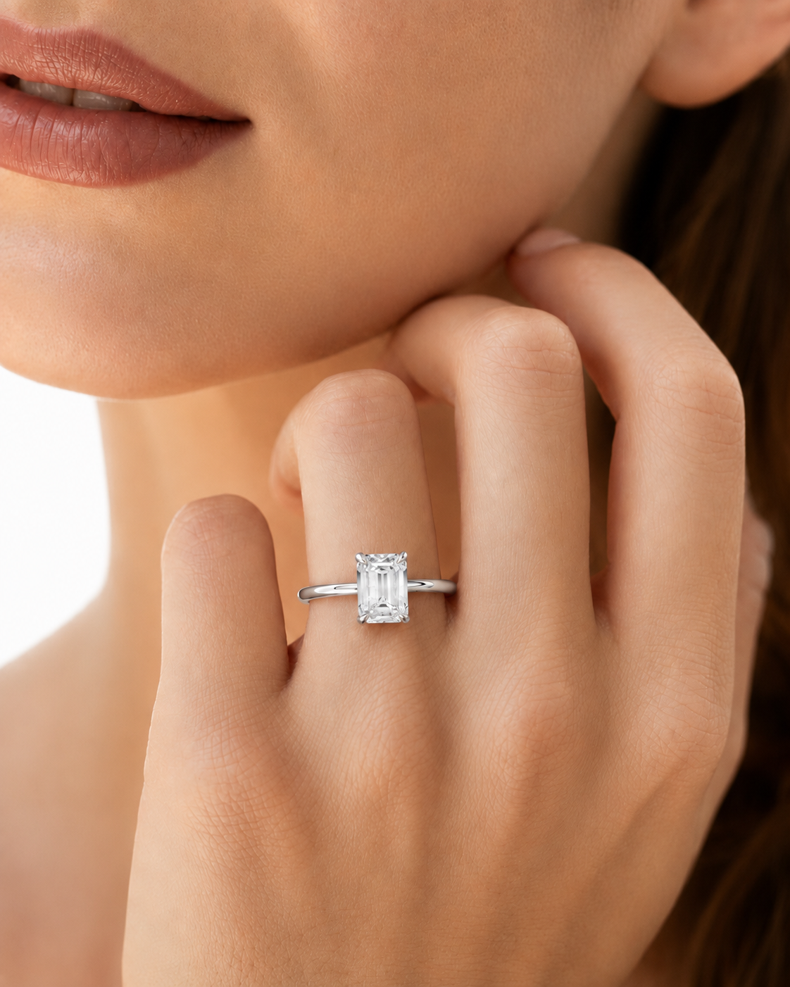 color_925_SIL,color_935_ARG,color_10K_WG, color_14K_WG &&A close-up lifestyle shot of a model wearing a silver engagement ring with a rectangular baguette-cut diamond. The ring is shown on her finger, with her hand resting near her chin against a bright, clean background.
