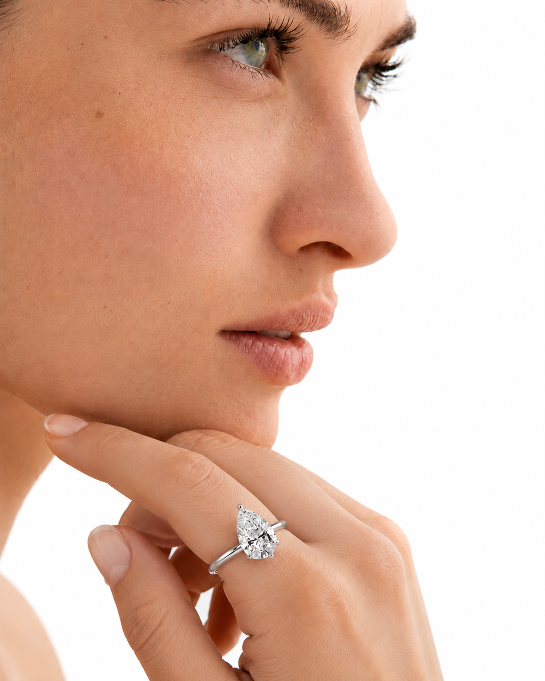 color_925_SIL,color_935_ARG,color_10K_WG, color_14K_WG &&A close-up side profile of a woman wearing a silver-toned ring with a marquise-cut clear gemstone on her finger, set against a bright white background.