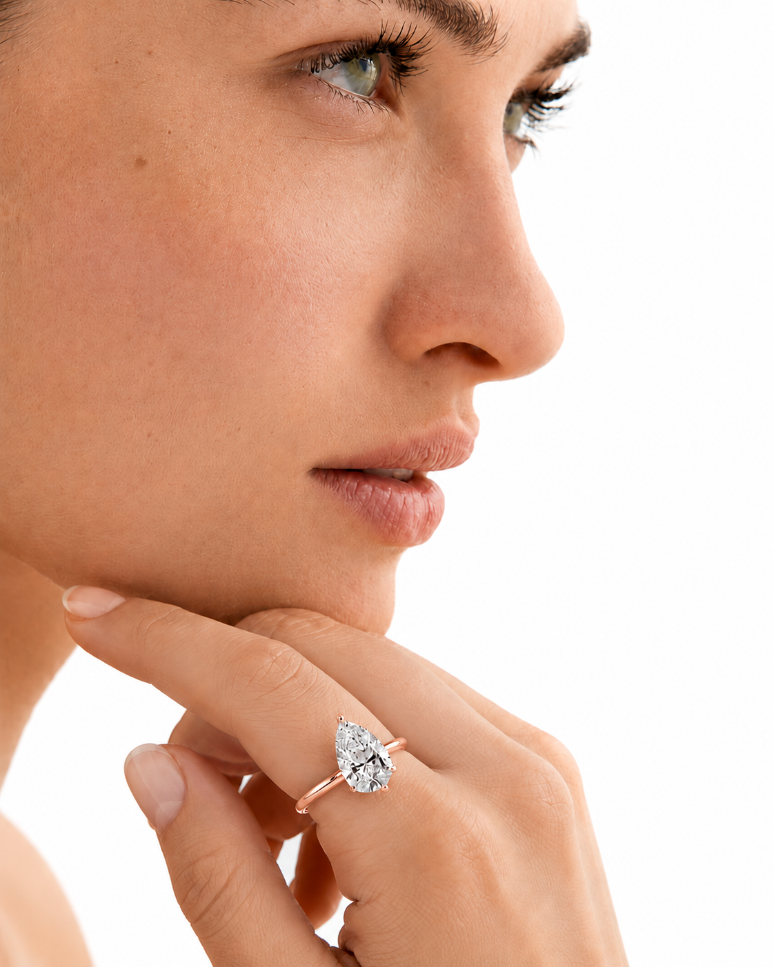 color_10K_RG, color_14K_RG &&A close-up side profile of a woman wearing a rose gold ring with a pear-cut clear gemstone on her finger, set against a solid white background.