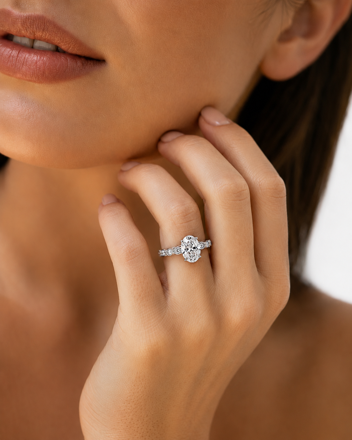 color_925_SIL,color_935_ARG,color_10K_WG, color_14K_WG &&A close-up lifestyle shot of a woman wearing a silver-toned diamond engagement ring on her finger, with her hand resting near her chin.
