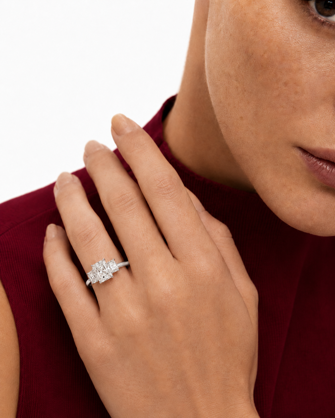 color_925_SIL,color_935_ARG,color_10K_WG, color_14K_WG &&A close-up lifestyle shot of a woman wearing a silver-toned diamond engagement ring on her hand, dressed in a deep burgundy top against a clean white background.