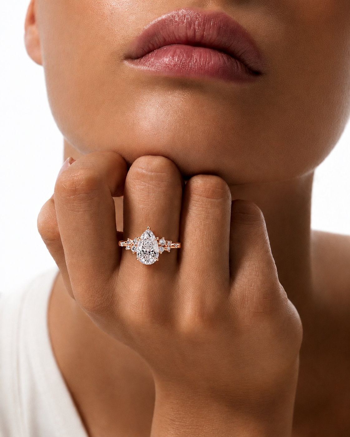 color_10K_RG, color_14K_RG &&A close-up lifestyle shot of a model wearing a rose gold ring with a pear-cut clear center stone and small side stones on her finger.