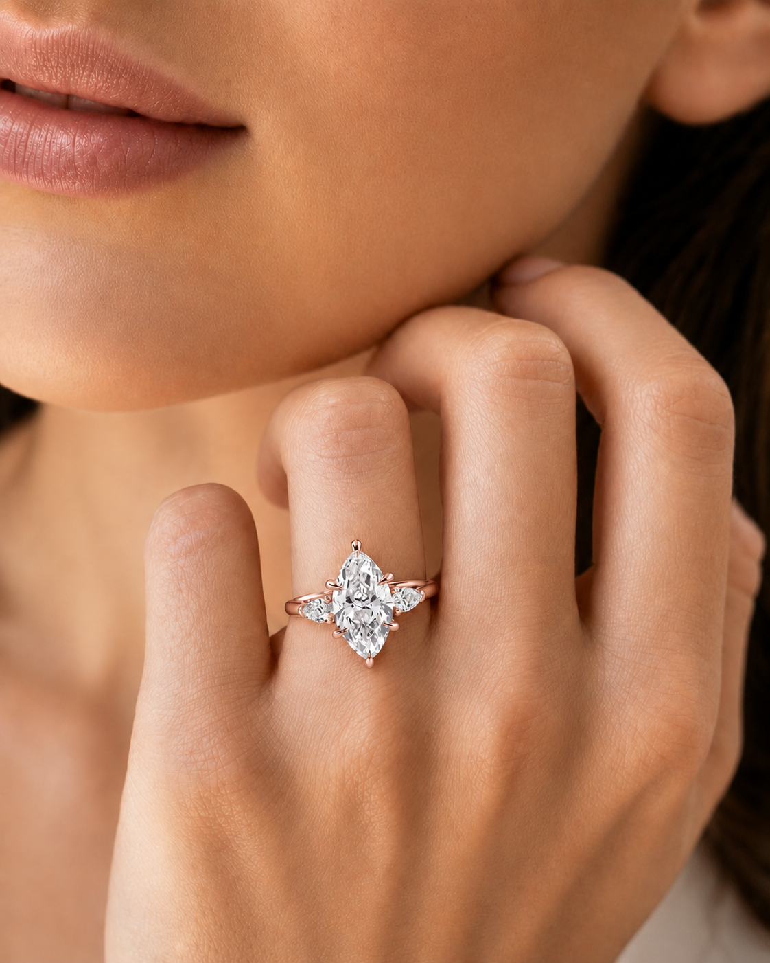 color_10K_RG, color_14K_RG &&A close-up lifestyle shot of a model's hand wearing a rose gold ring with a marquise-cut diamond center stone and smaller round diamonds.