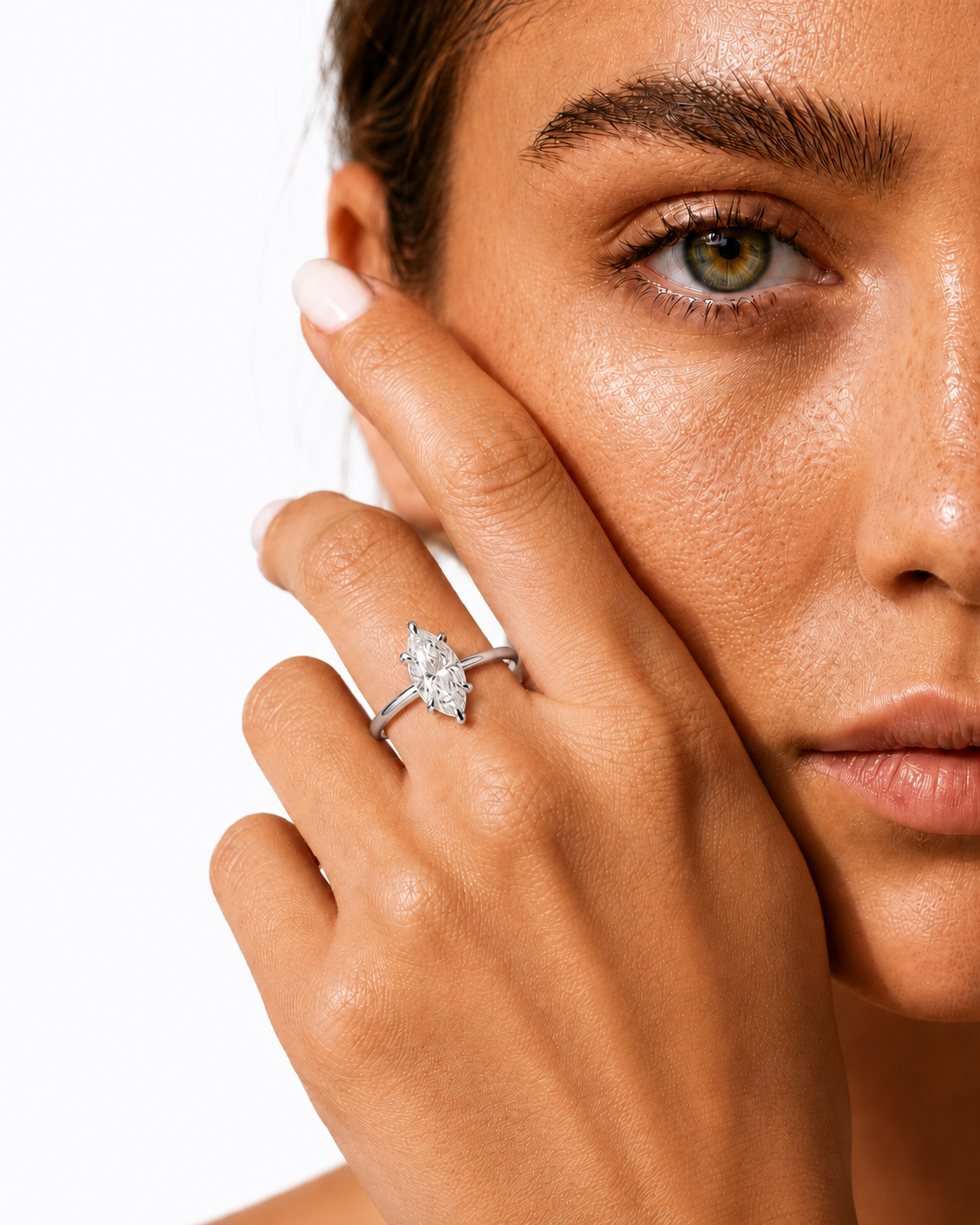 color_925_SIL,color_935_ARG,color_10K_WG, color_14K_WG &&A close-up of a model's face and hand wearing a silver marquise-cut diamond engagement ring against a clean white background.